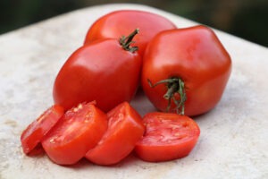 Three red 'Amish Paste' tomatoes and four thick tomato slices on a granite surface
