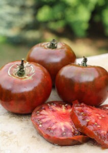 Three deep red-purple 'Paul Robeson' tomatoes and two tomato slices on a smooth granite surface