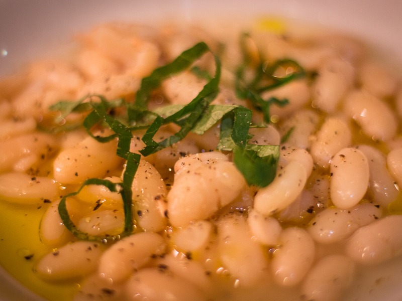 A dish of cooked white beans with seasoning and a green garnish